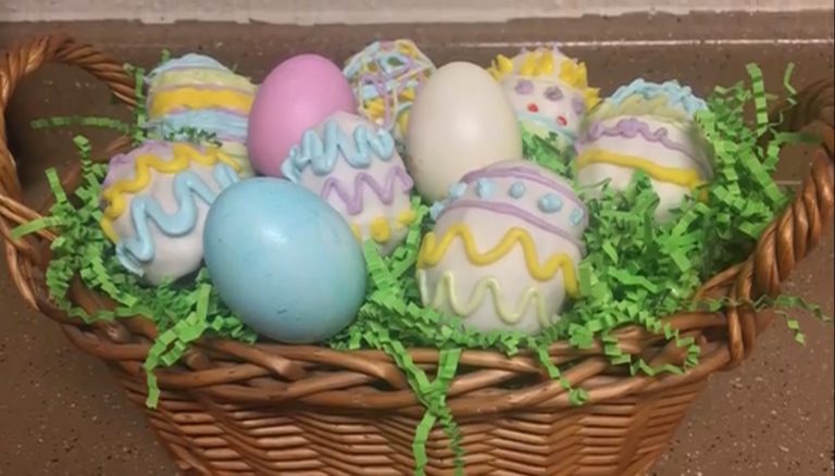 Wicker basket filled with fake grass with decorated eggs on top made with cake.
